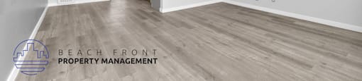 A spacious room with wooden flooring and a logo for Beach Front Property Management in the corner.