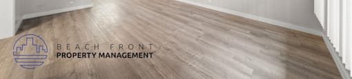 A spacious room with wooden flooring and white walls, managed by Beach Front Property Management.