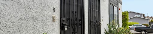A black gate with the letter B above it is on a white wall.