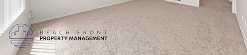 A spacious room with carpeted floor and white walls, with a logo for Beach Front Property Management in the bottom left corner.