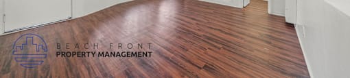 A room with wooden floors and white walls, with a logo for Beach Front Property Management in the bottom left corner.