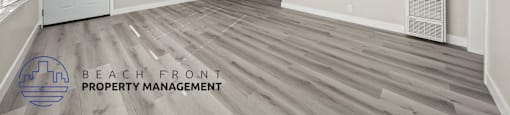 A spacious room with wooden flooring and a logo for Beach Front Property Management.