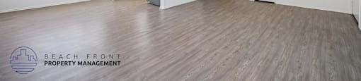 A spacious room with wooden flooring and white walls, featuring a kitchen area with white cabinets and a refrigerator.
