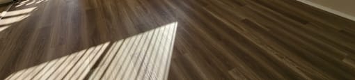 A room with wooden flooring and a view of a fenced area outside through the window.