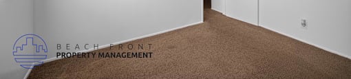 A room with white walls and brown carpeting, with a logo for Beach Front Property Management in the bottom left corner.
