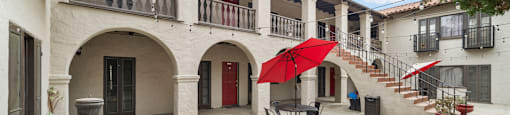 A courtyard with a table and chairs and a red umbrella.