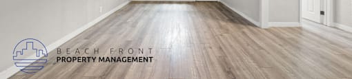 A spacious room with wooden flooring and white walls, with a logo for Beach Front Property Management in the bottom left corner.