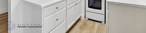A white kitchen with a stove, sink, and cabinets.