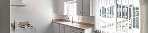 A kitchen with white cabinets and a window with blinds.