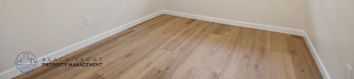 A room with wooden floors and a window showing a fence and trees outside.