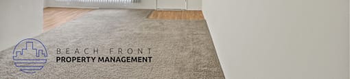 A room with a carpet on the floor and a logo for Beach Front Property Management in the corner.
