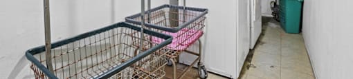 A white wall with a shopping cart in front of a washing machine and a dryer.