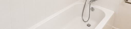 A white bathtub with a shower head and a window with blinds.