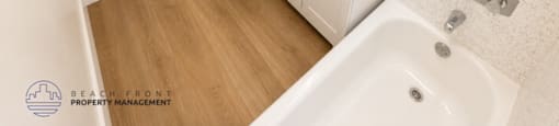 A white bathroom with a wooden floor and a white tub.