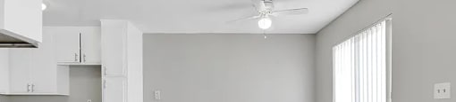 A spacious kitchen and living room with white cabinetry and a ceiling fan.
