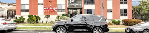 A black SUV is parked in front of a building with a sign that says "Now Leasing.".