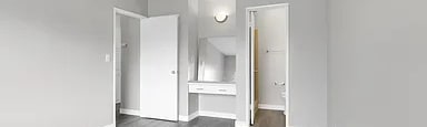 A room with a ceiling fan and light, hardwood floors, and white walls with two doors.
