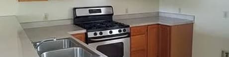 A kitchen with a stove, sink, and cabinets.
