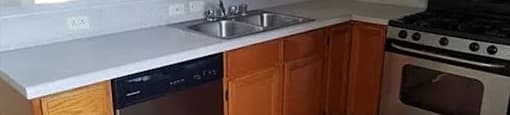 A kitchen with wooden cabinets and a stainless steel dishwasher.