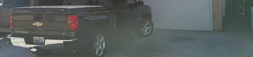 A black Chevy truck is parked in front of a tan house.