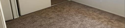 A room with carpeted floor and a window with blinds.