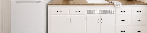 A white refrigerator stands next to a kitchen counter with a bowl of fruit on it.