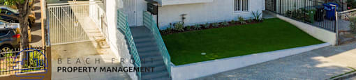 A white two-story house with a green staircase and a sign that says "BEACH FRONT PROPERTY MANAGEMENT".