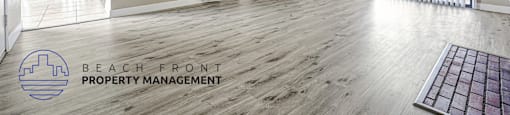 A spacious room with wooden flooring and a logo for Beach Front Property Management in the corner.