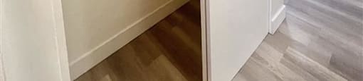 A white closet with shelves and a doorway leading to a room with a window and air conditioner.