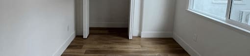 a room with white walls and wood floors and a door to a closet