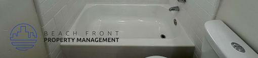 A white tiled bathroom with a window and a bathtub.