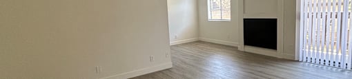 A room with a wooden floor and a window with blinds.