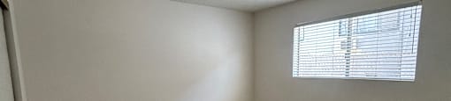 A room with a wooden floor and a window with blinds.