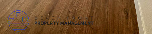 A room with wooden floors and white walls, with a logo for Beachfront Property Management in the bottom left corner.