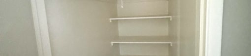 a walk in closet with white shelves and a wood floor