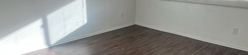 A room with wooden flooring and a window letting in sunlight.