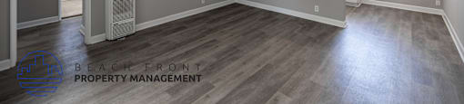 A spacious room with wooden flooring and a window with blinds.