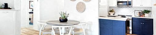 A white dining table with four chairs is in a kitchen with a blue cabinet.