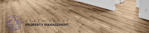 A spacious room with wooden flooring and white walls, with a logo for Beach Front Property Management in the bottom left corner.