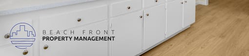 A kitchen with white cabinets and a logo for Beach Front Property Management.