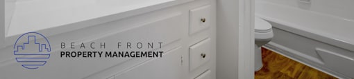 A white bathroom with a sink, mirror, and a logo for Beach Front Property Management.