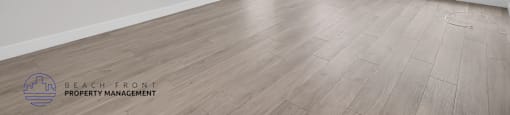 A spacious room with wooden flooring and a window with blinds.