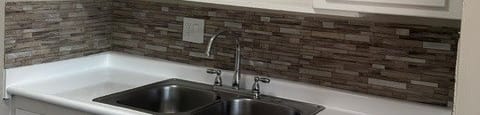 A kitchen with white cabinets and a stone backsplash.