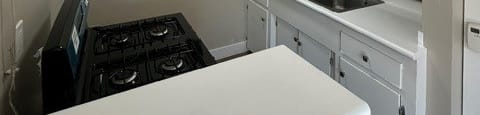 A small kitchen with a white counter top and a black stove.