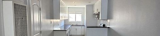 a renovated kitchen with white cabinets and a wooden floor