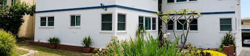 A white two-story building with a blue stripe on the roof and a garden in front.