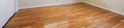 an empty room with wooden floors and two windows