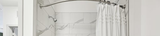 A white bathroom with a marble tile wall and a white tub.