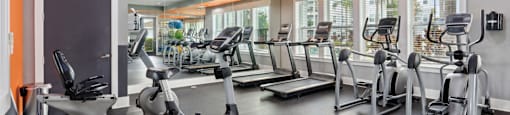 A gym with a variety of equipment including treadmills, stationary bikes, and elliptical machines.