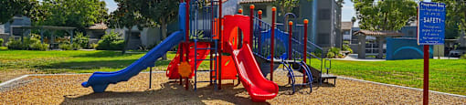 A playground with a blue umbrella and a red slide.